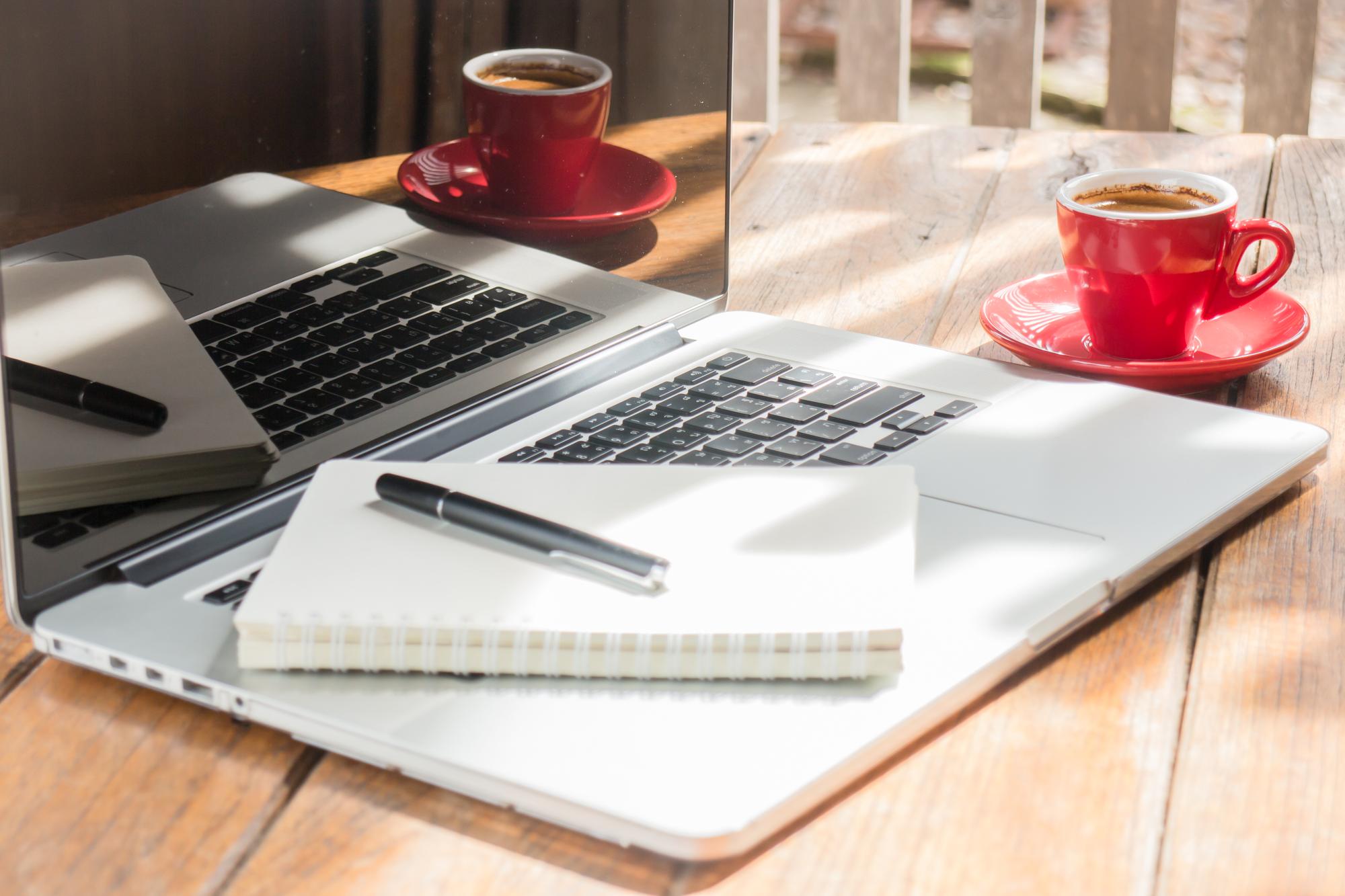 Arbeitsplatz: Laptop, Notizbuch und Kaffeetasse